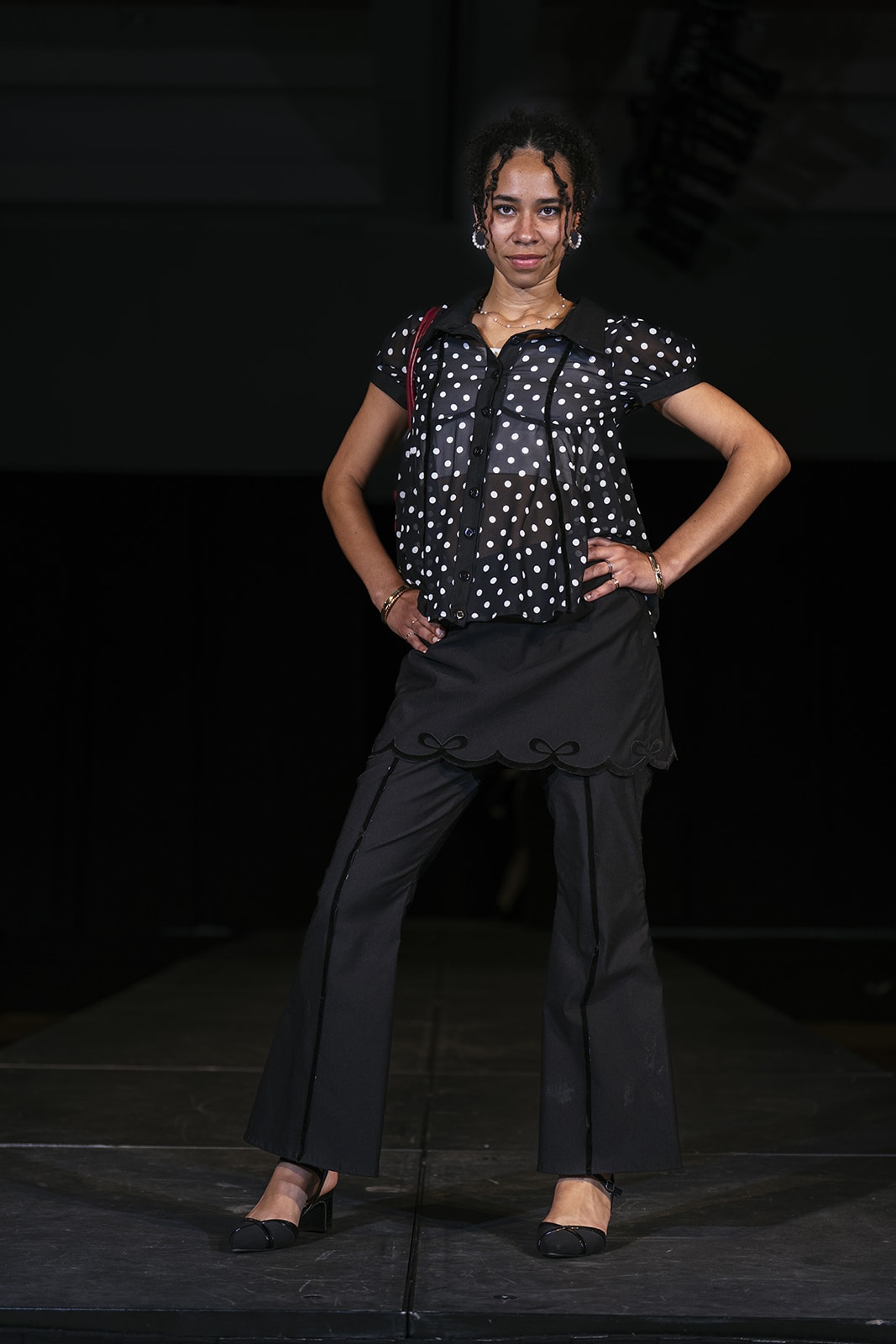 Model on the runway in a two piece black outfit with pants and a shirt.