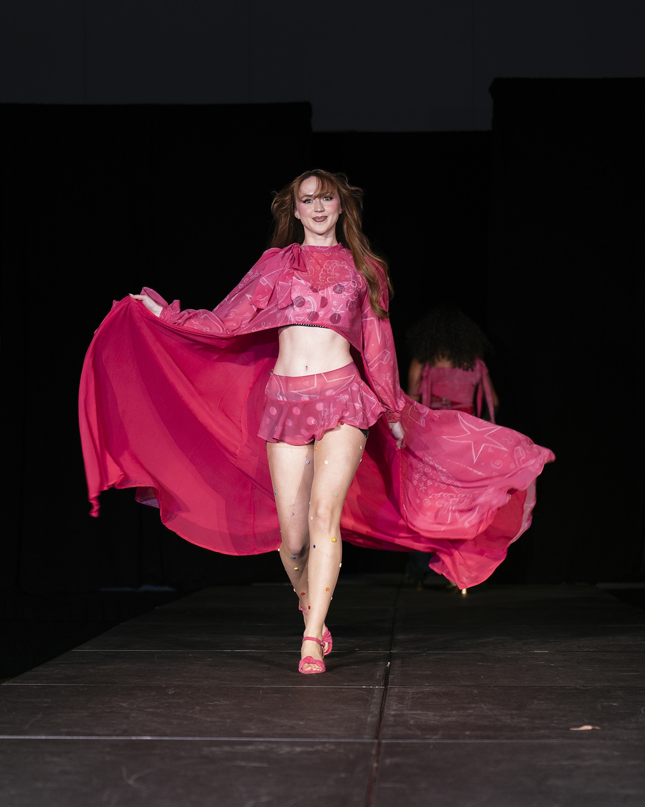 Model on the runway wearing a pink skirt and flowy top.