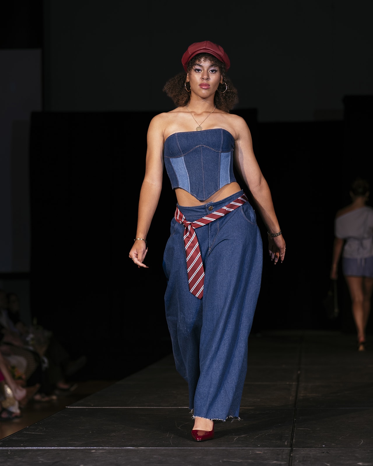 Model on the runway wearing a blue strapless top, blue skirt and a red and white striped belt.