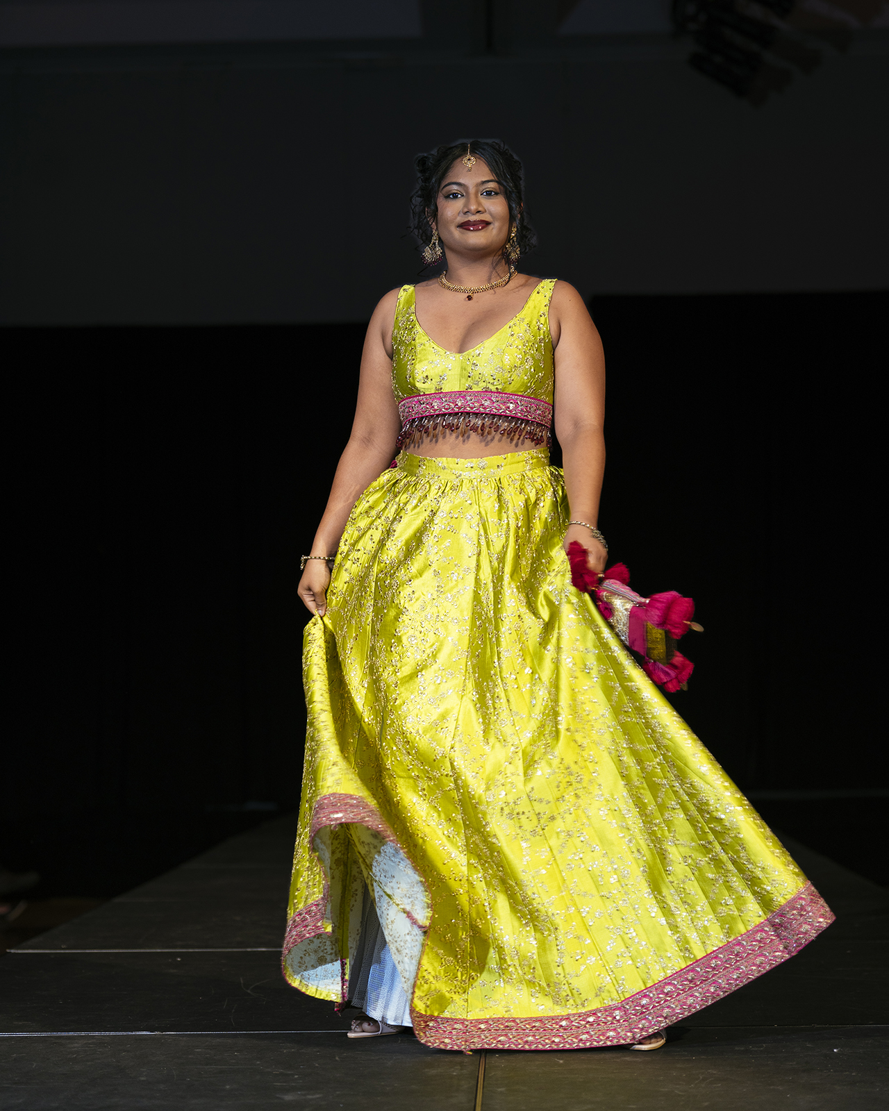 Model on the runway wearing a yellow skirt with red strip and a yellow top with red trim.
