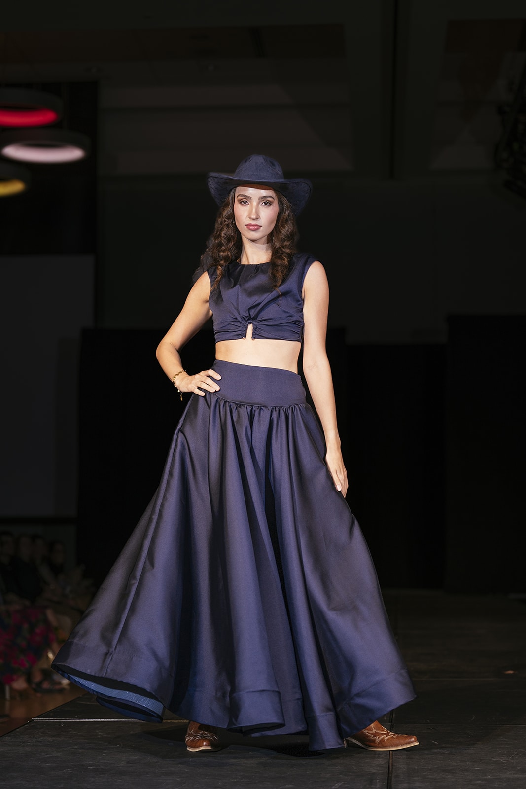 Model on the runway wearing a navy outfit consisting of a hat, top, skirt and pants.