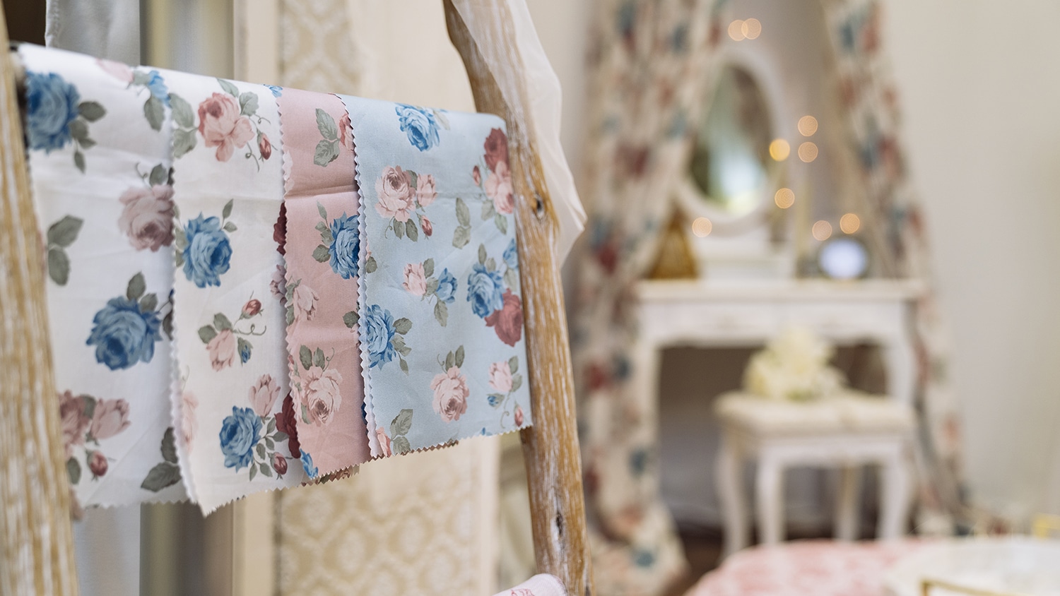 Floral print textiles hang off a wood ladder in the foreground while a vanity is in the background.