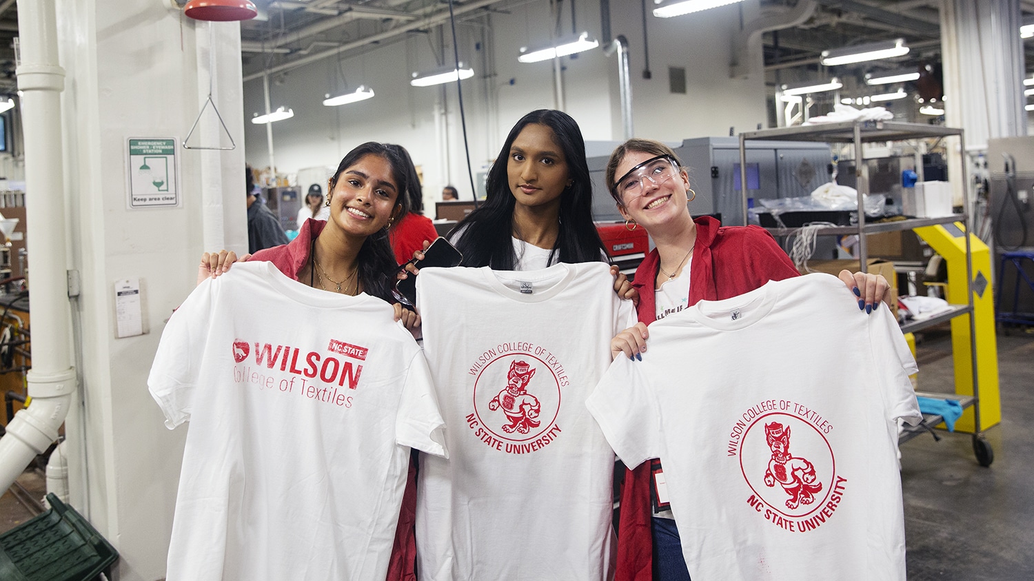Three students hold t-shirts while wearing lab coats.