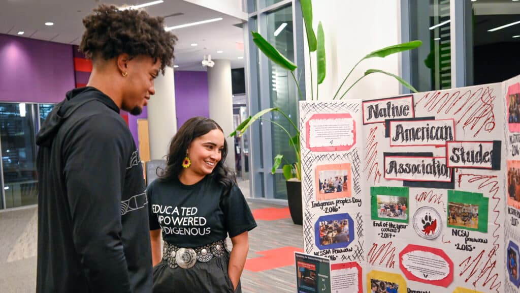 Two people look at a trifold poster board with the title "Native American Student Association."