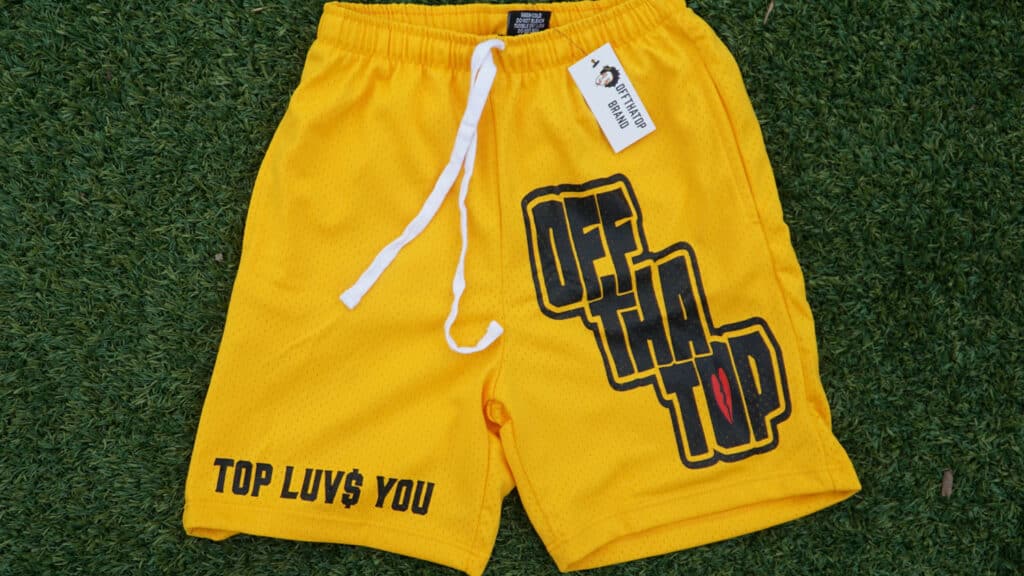 A pair of yellow athletic shorts with "Off Tha Top" and "Top Luv$ You" printed on the them.