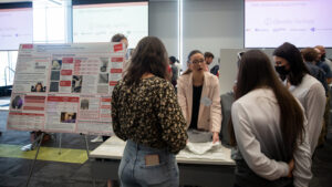 student presents poster to other students in library