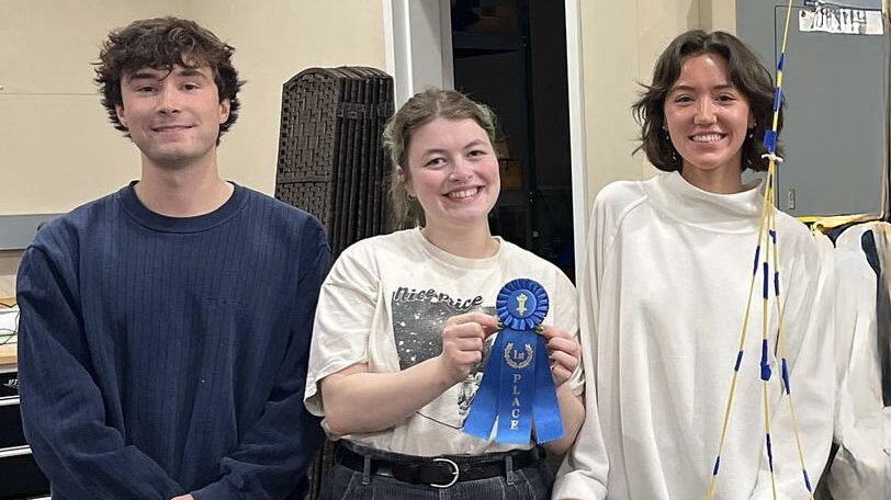 Team members stand in studio holding a first place ribbon.