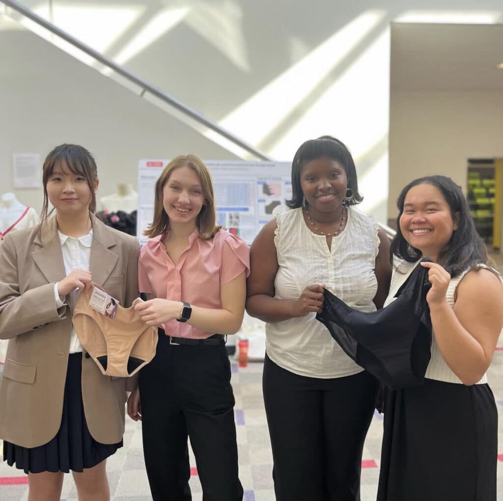 Team members hold up their underwear samples in front of their presentation posters. 