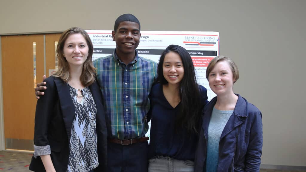 Darian Boyd and three others stand together smiling in front of a research poster. 

