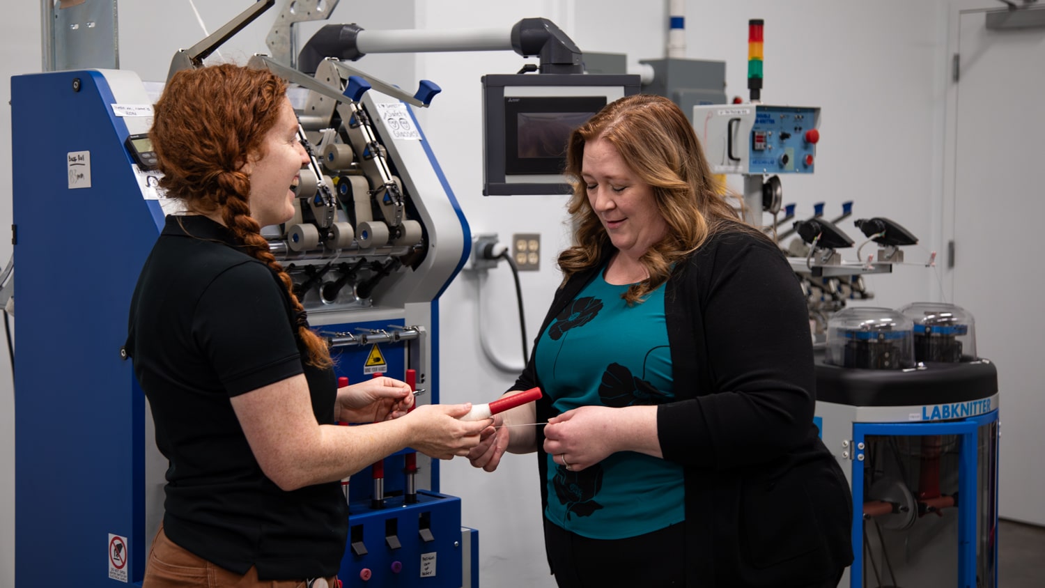 Bailey Knight hands a skein of yarn to Melissa Sharp in the Prototype Lab.