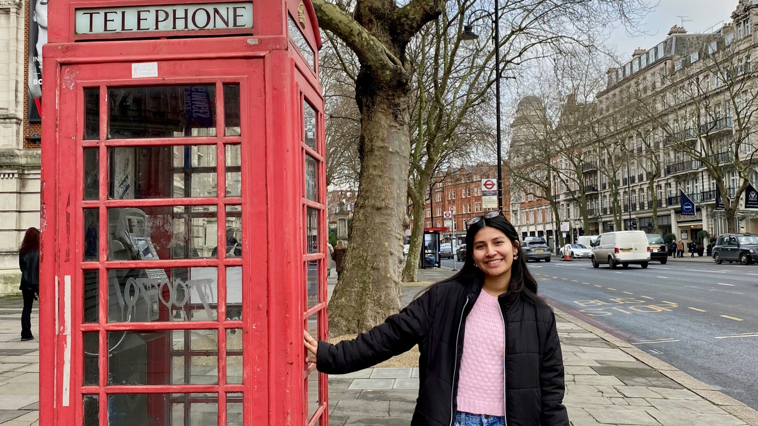 Student smiling while standing next to a red English phone booth.