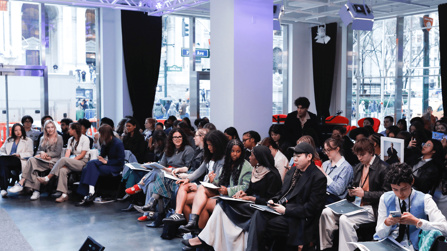 A large group of 2025 FSF Scholars sits holding notebooks and laptops awaiting a presentation.