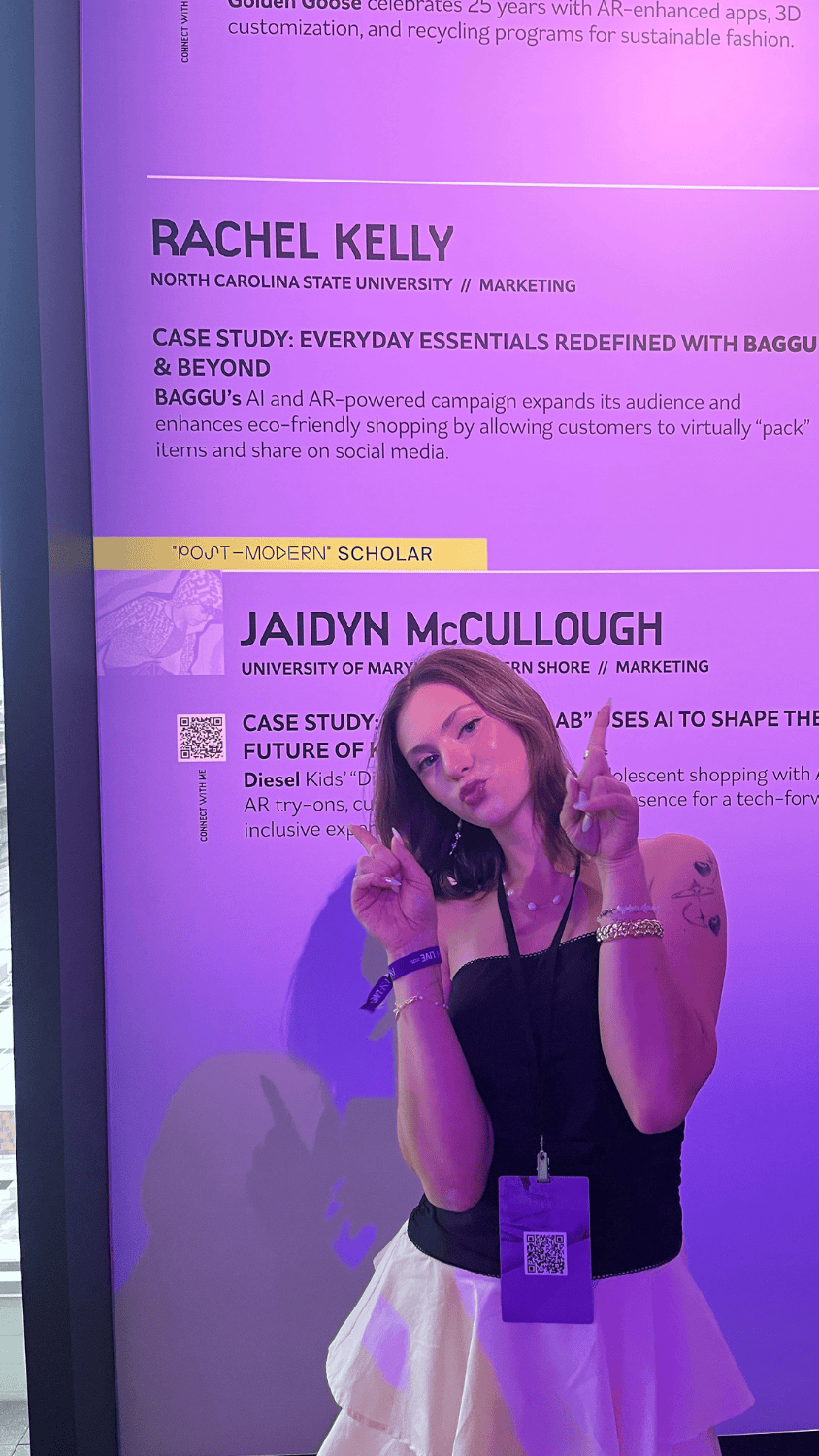 Rachel Kelly stands in front of a large screen pointing at her name displayed with her case study title.
