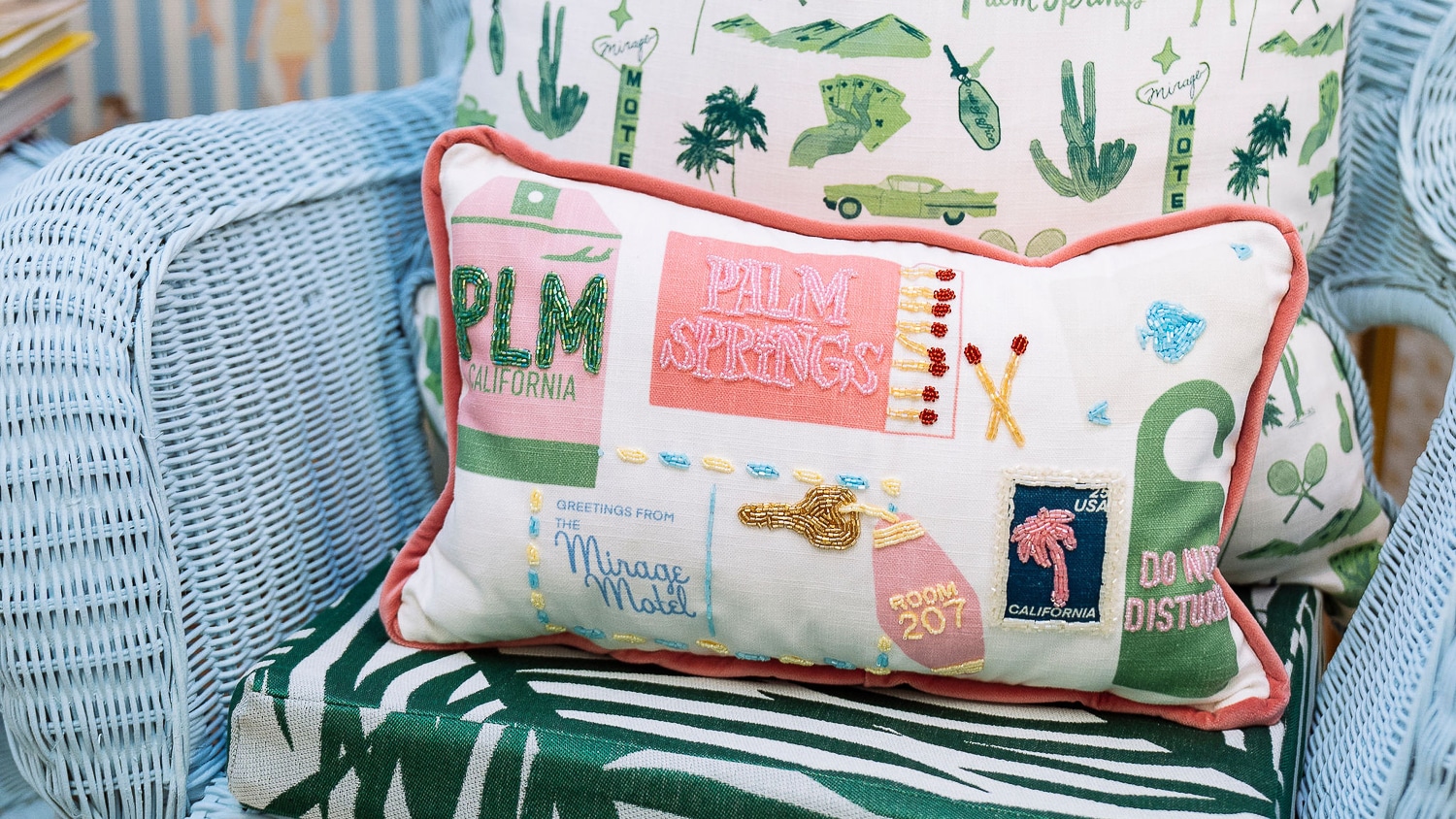 A decorative pillow from Beasley Gordon's capstone collection. It has green and pink designs themed around Palm Springs, like a matchbox and a retro pink hotel key.