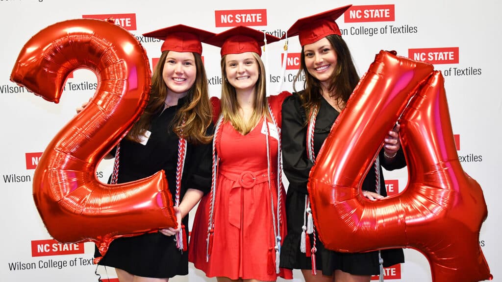 Meredith smiles while hold balloons alongside her two friends.