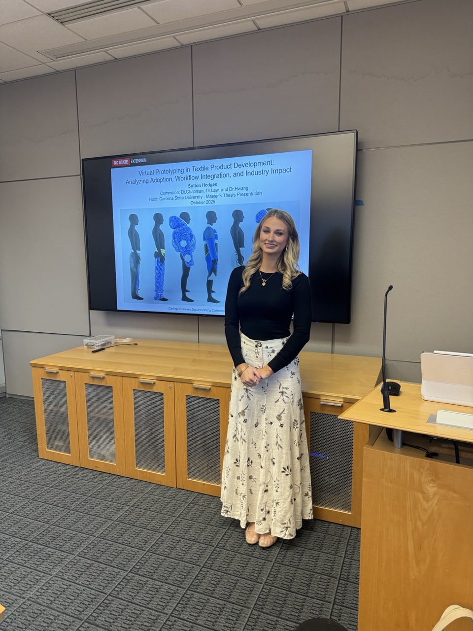 Sutton Hodges stands and smiles in front of a large screen displaying her thesis presentation titled 