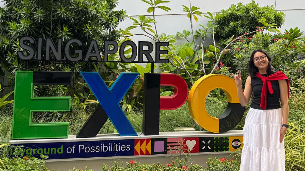 Student smiling while standing next to the Singapore Expo sign.