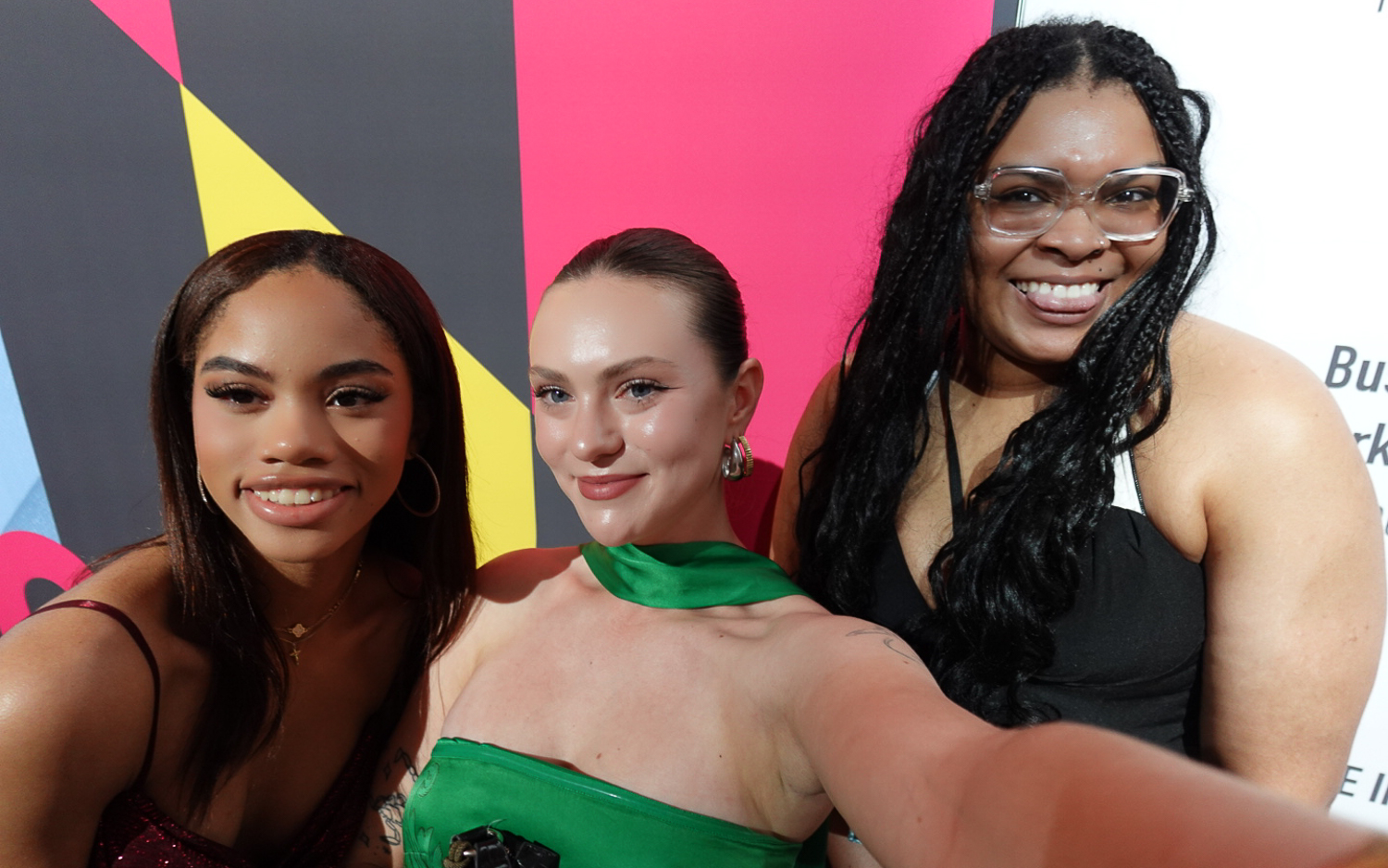 Kyla Perry, Rachel Kelly and Celia Fennell (left to right) pose for a selfie in front of a colorful geometric background.