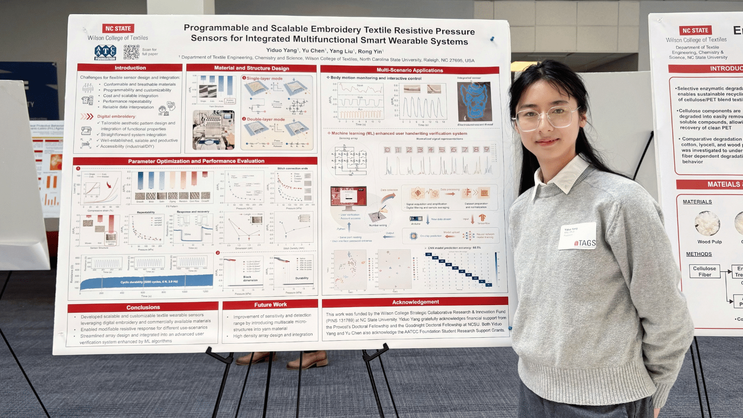 Yiduo Yang stands next to her research poster at the Textiles Research Symposium. She has long black hair behind her shoulders and thin glasses, and wears a grey sweater with a white button-up underneath. The poster is jammed with small words and diagrams.