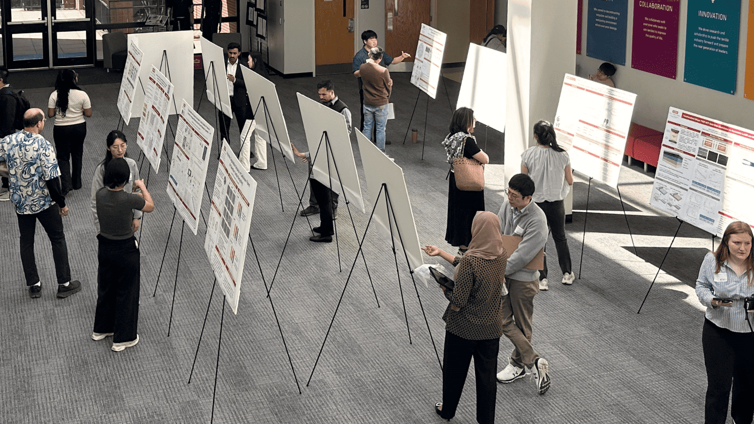 The Textiles Research Symposium underway, with community members viewing rows of research posters in the lobby of the Textiles Complex.