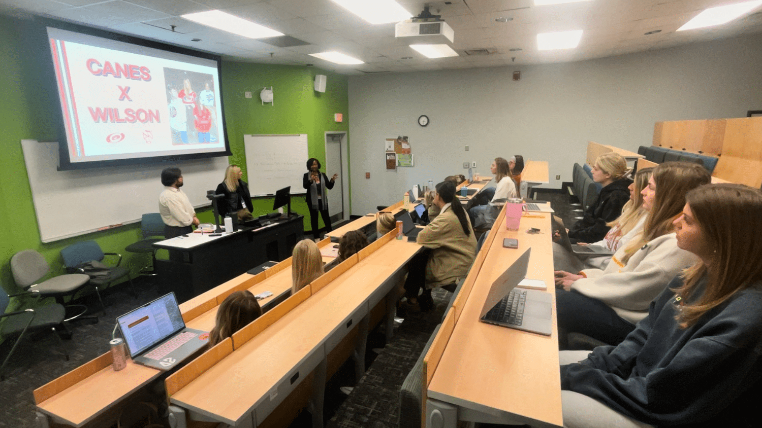 Dr. Matthews speaks to a classroom of students with a screen that says Canes x Wilson