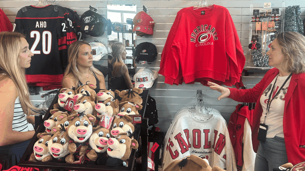 Two students stand in a Carolina Hurricanes shop with merchandise talking to a marketing employee