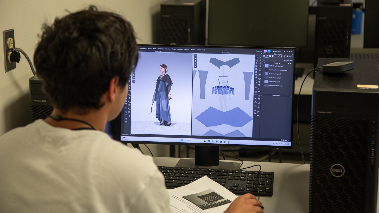 A high school student works on a design on a monitor in on of the computer labs in the Textiles Campus. The camera is pointed over their shoulder at the computer screen, where a 3D model wears the garments which are broken down on the left side of the screen. The student has short, dark hair and wears a white t-shirt.