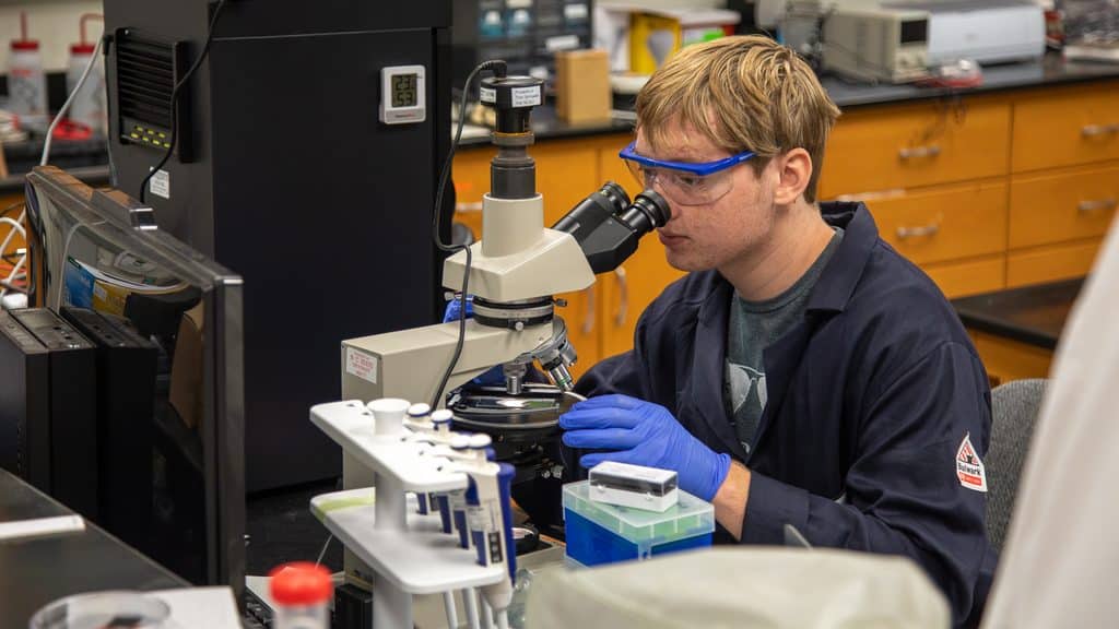 Third year student Owen Rector conducting research with scientific materials in a lab wearing goggles and gloves.