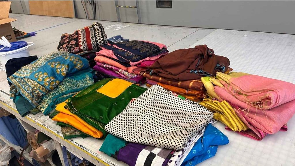Piles of donated Saris with different colors and patterns folded on a table.