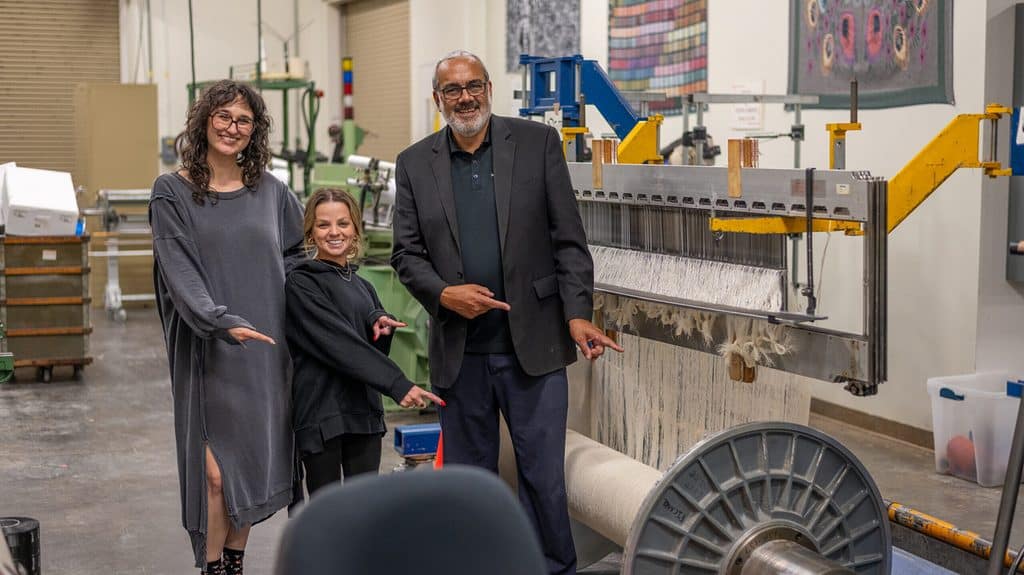 Dr. Andre West and 2 individuals smiling and pointing at a machine