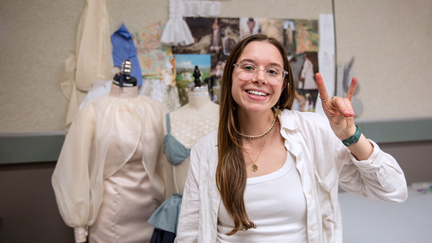 Lilly Barozzini standing in front of two mannequins with her designs and a mood board.