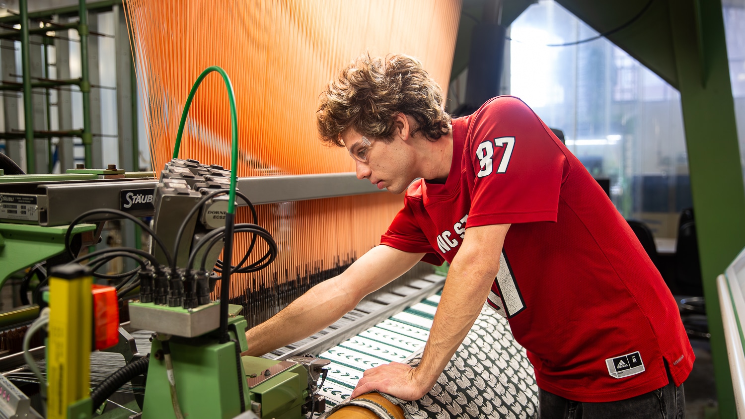 Student inspects material on weaving machine.