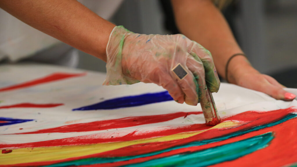 A student's hand oil painting a piece of white fabric.