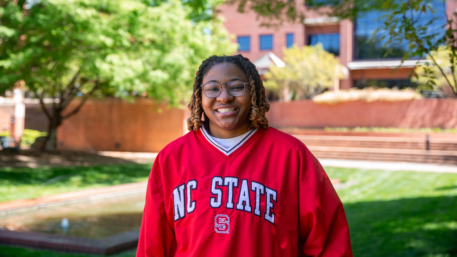 Jordan Everett wears an NC State windbreaker and stand smiling. Th Wilson College of Textiles courtyard is visible in the background. 